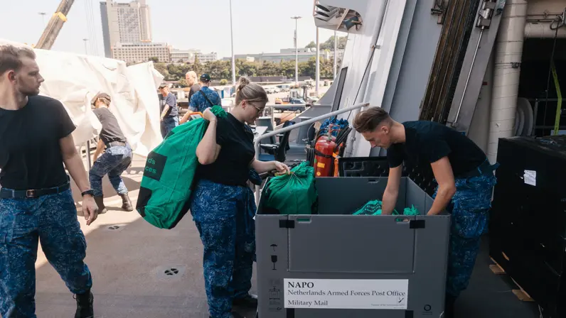 2 marinemensen snuffelen op dek marineschip in een kist met postzakken.