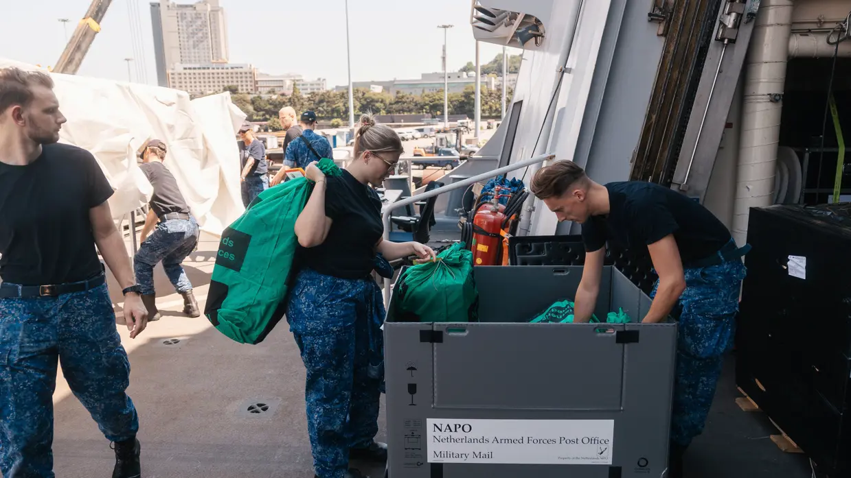 2 marinemensen snuffelen op dek marineschip in een kist met postzakken.