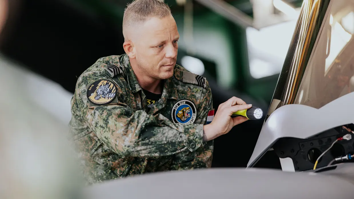 Glenn Afman in groen vlekkenpak inspecteert van dichtbij met een zaklamp een F-35. 