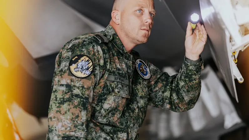 Glenn Afman in groen vlekkenpak inspecteert van dichtbij met een zaklamp een F-35.