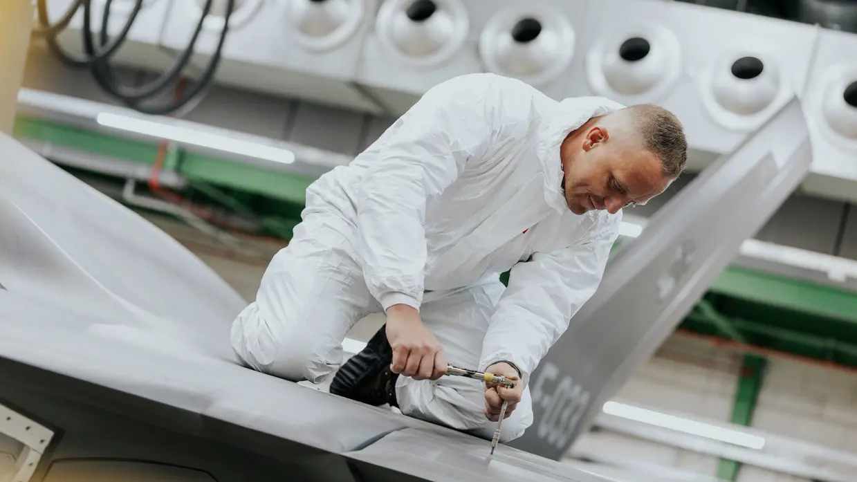 Glenn Afman in een witte overal aan het werk bovenop een F-35-vleugel. 