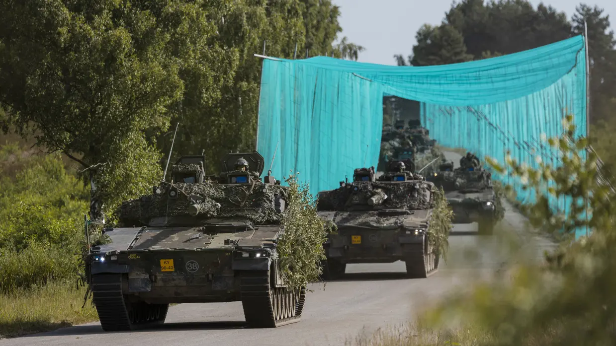 Leopard 2A8-gevechtstanks rijden tijdens oefening Fighter Lion onder camouflagenetten door over een bosweg.