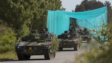 Leopard 2A8-gevechtstanks rijden tijdens oefening Fighter Lion onder camouflagenetten door over een bosweg.