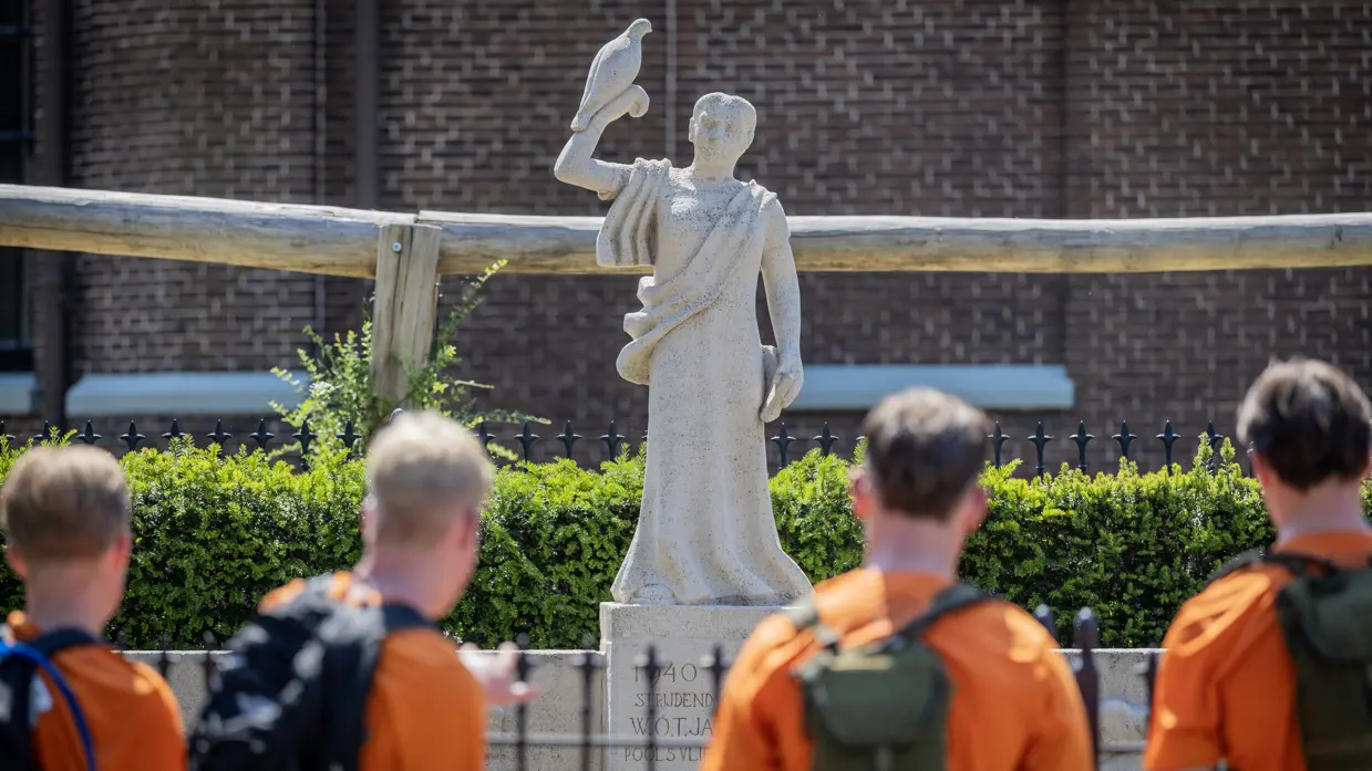 Jongeren voor een monument met een oranje t-shirt.