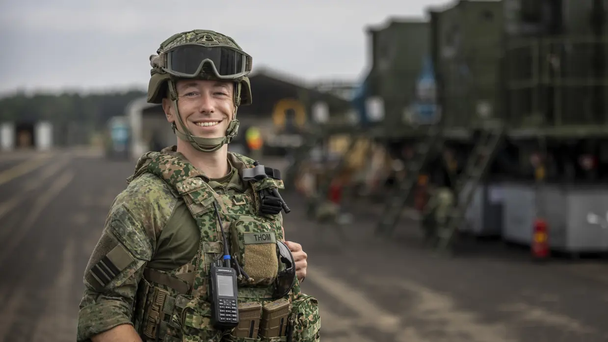 Militair met vest en helm op staat op taxibaan vliegbasis.