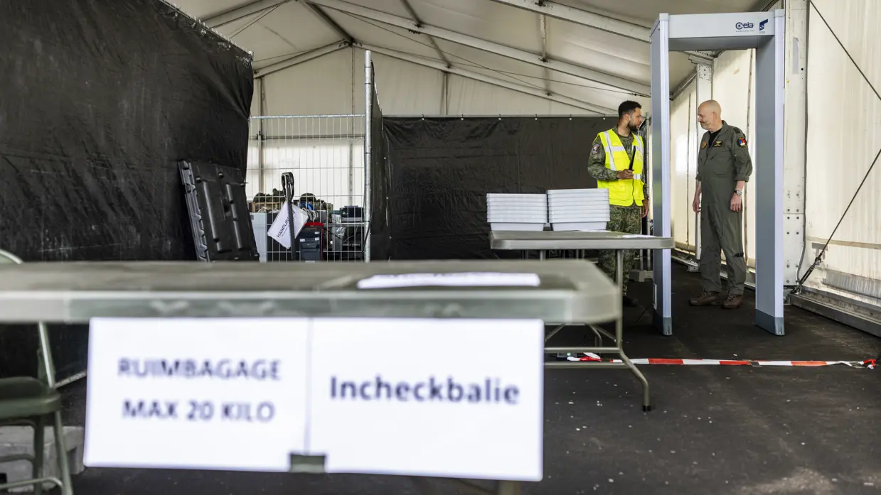Militair in geel hesje geeft andere militair uitleg bij incheckbalie op tijdelijke vliegbasis.