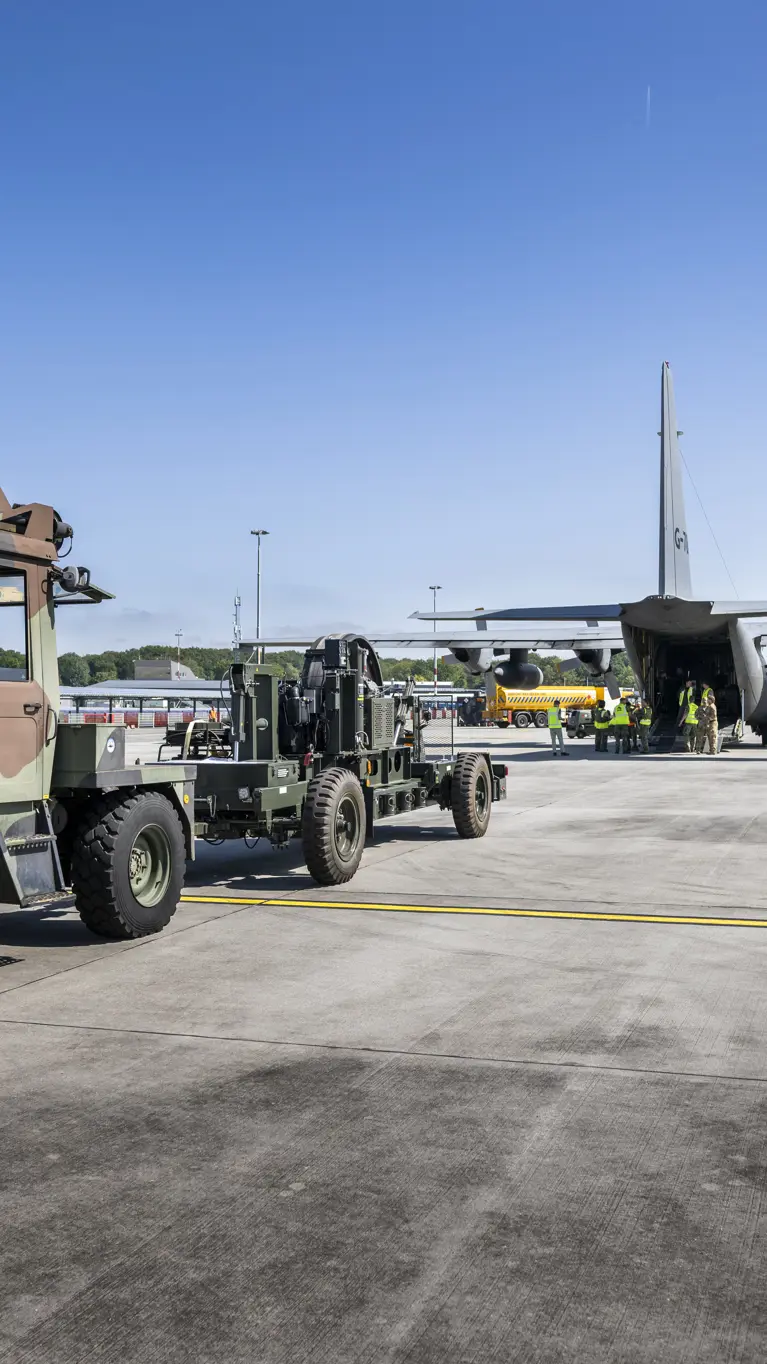 Truck en oplegger staan op een vliegveld klaar met materieel om Hercules-transportvliegtuig in te laden.