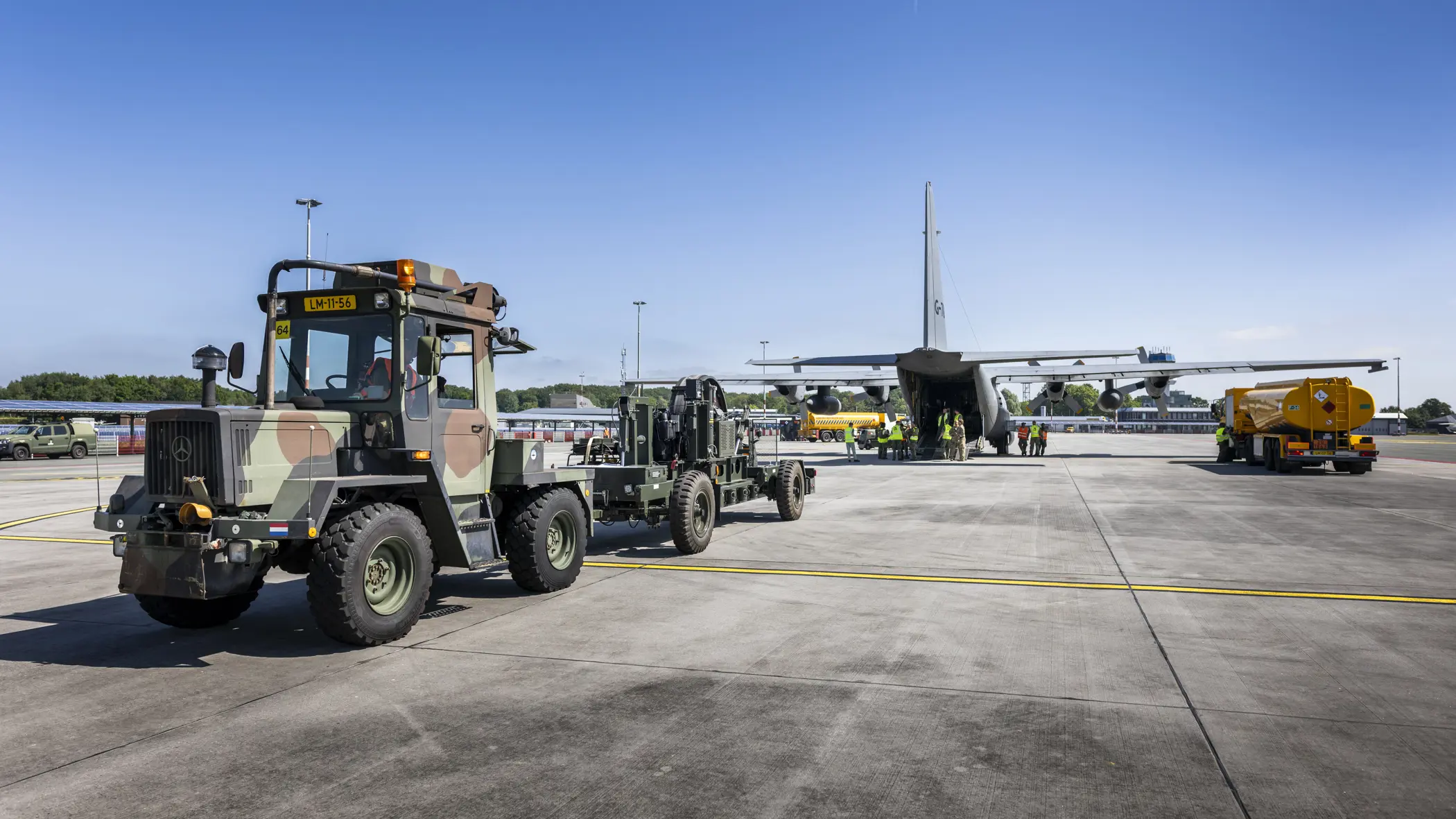 Truck en oplegger staan op een vliegveld klaar met materieel om Hercules-transportvliegtuig in te laden.