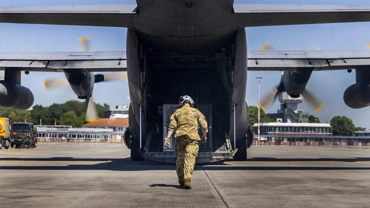 Militair loopt richting openstaande laadklep van C-130 Hercules-transportvliegtuig.