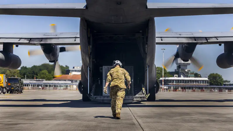 Militair loopt richting openstaande laadklep van C-130 Hercules-transportvliegtuig.