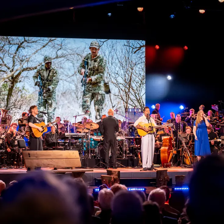 Drie solisten spelen en zingen op het podium. In de achtergrond het orkest van de luchtmacht.