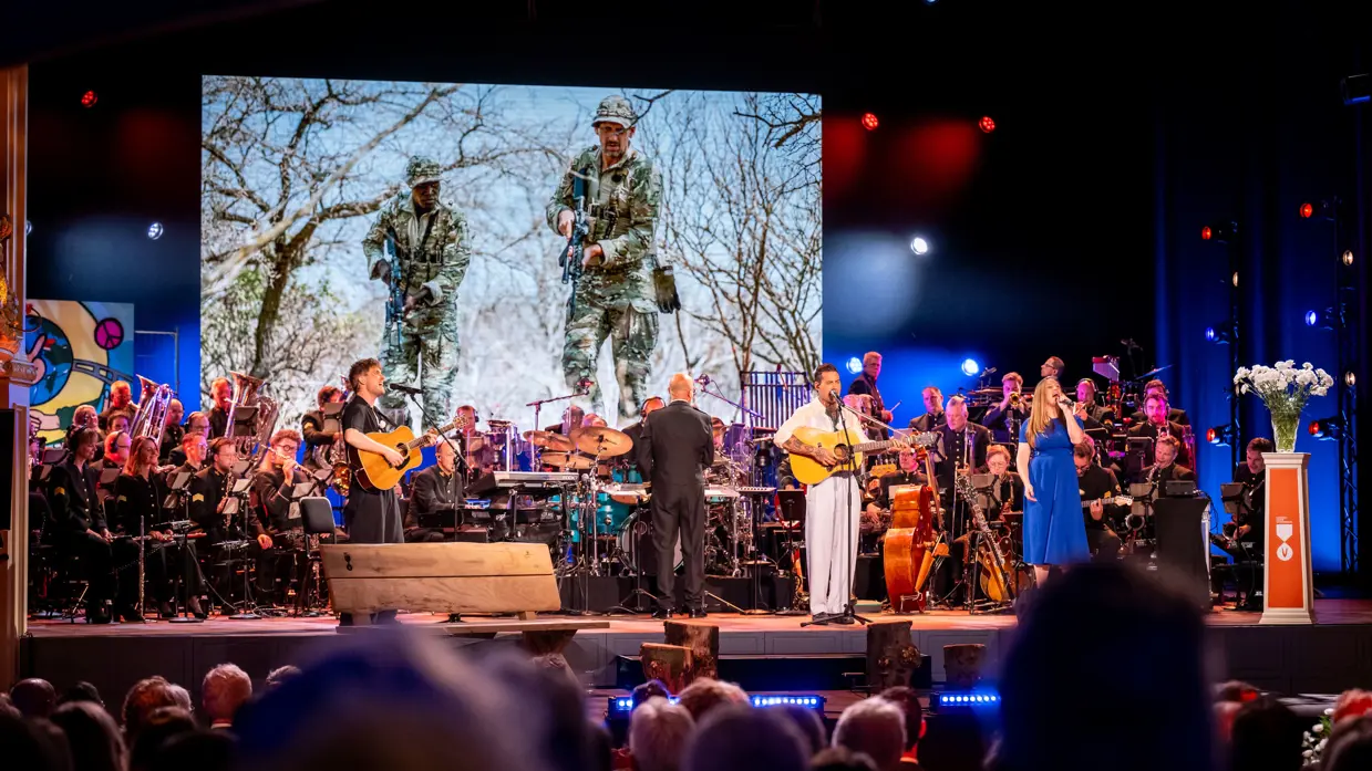 Drie solisten spelen en zingen op het podium. In de achtergrond het orkest van de luchtmacht.