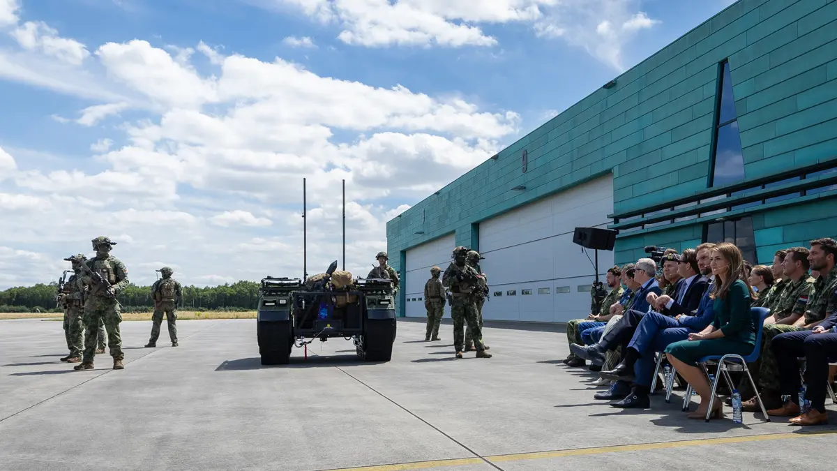 Militairen begeleiden een zelfrijdend voertuig met aan de rechterkant een publiek.