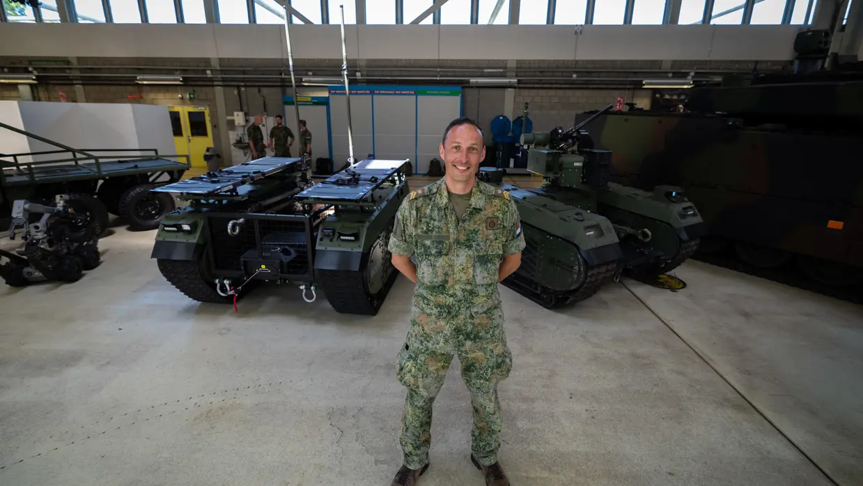 Een militair poseert voor twee zelfrijdende voertuigen.