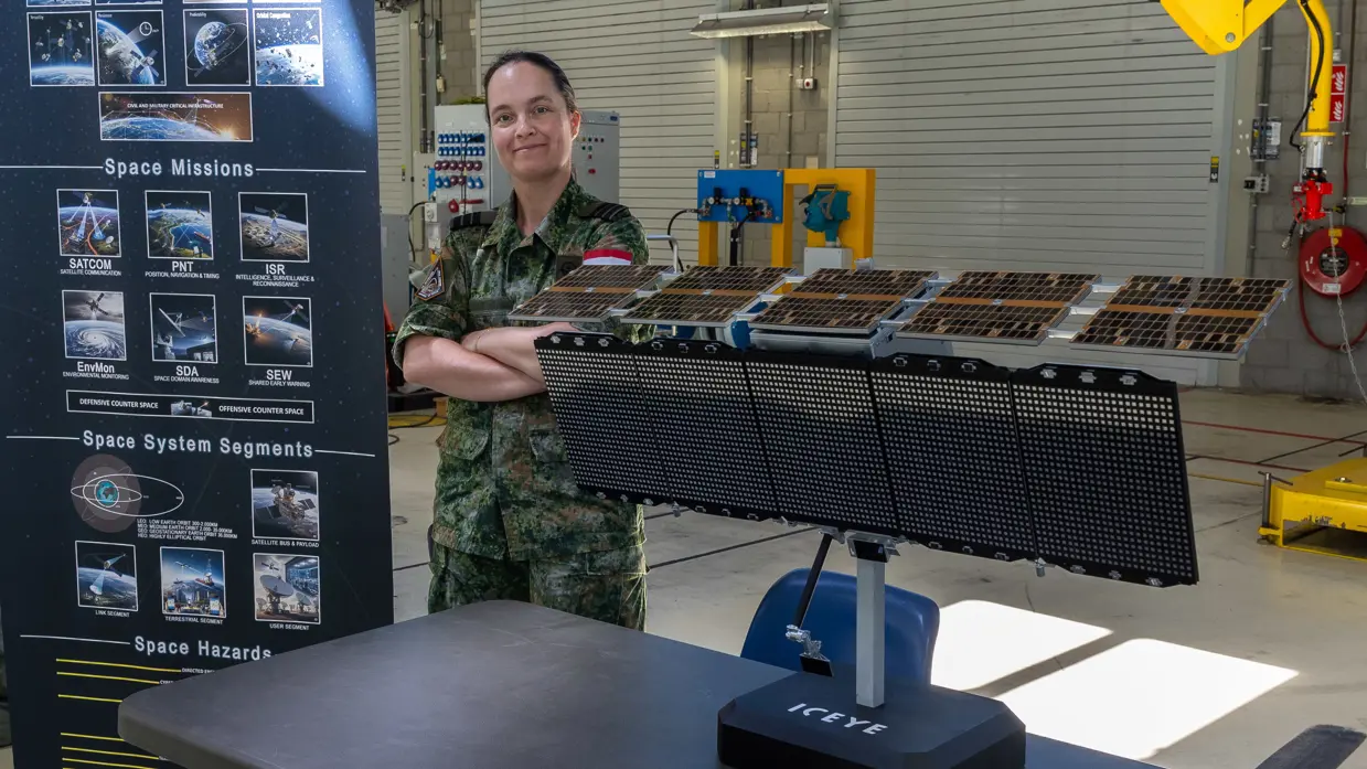 Een militair poseert naast een model van de nieuwe satelliet.