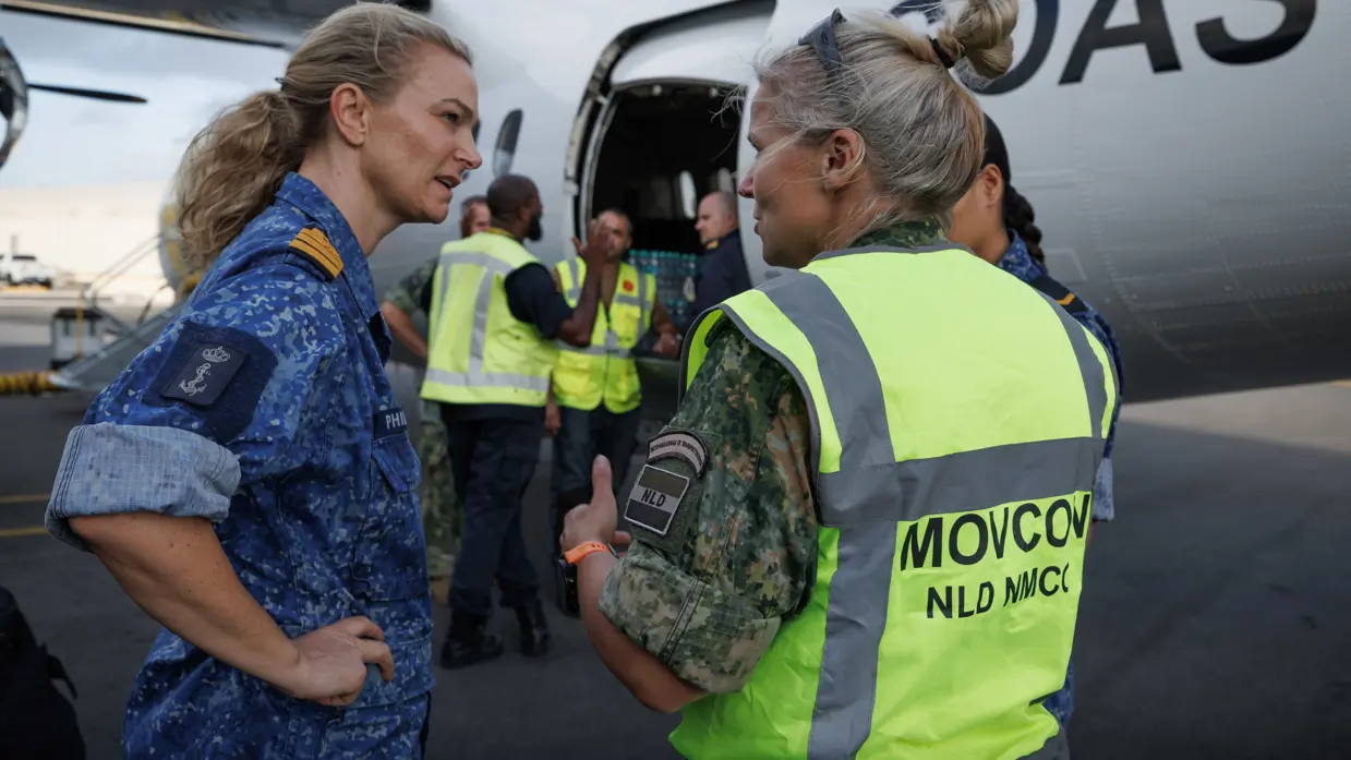 Militairen staan te overleggen naast een vliegtuig.