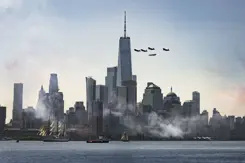 De Amerikaanse stad New York. Ervoor varen schepen en erboven vliegen militaire toestellen.