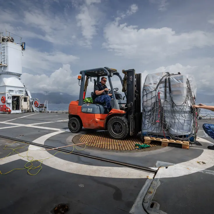 Een voorheftruck op het achterdek zet een pallet met waterflessen neer.
