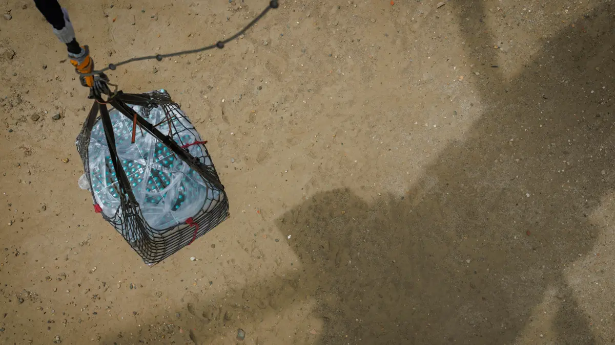 Een pallet met drinkwater hangt boven de grond aan een helikopter.