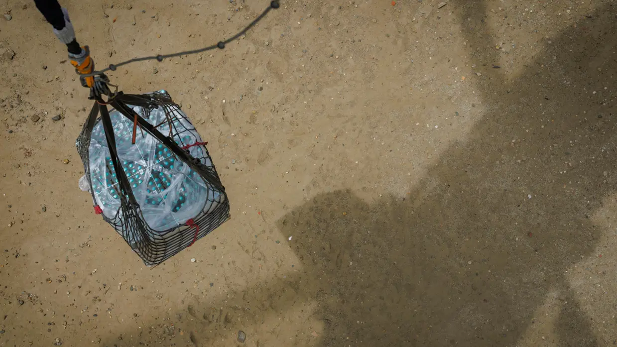 Een pallet met drinkwater hangt boven de grond aan een helikopter.