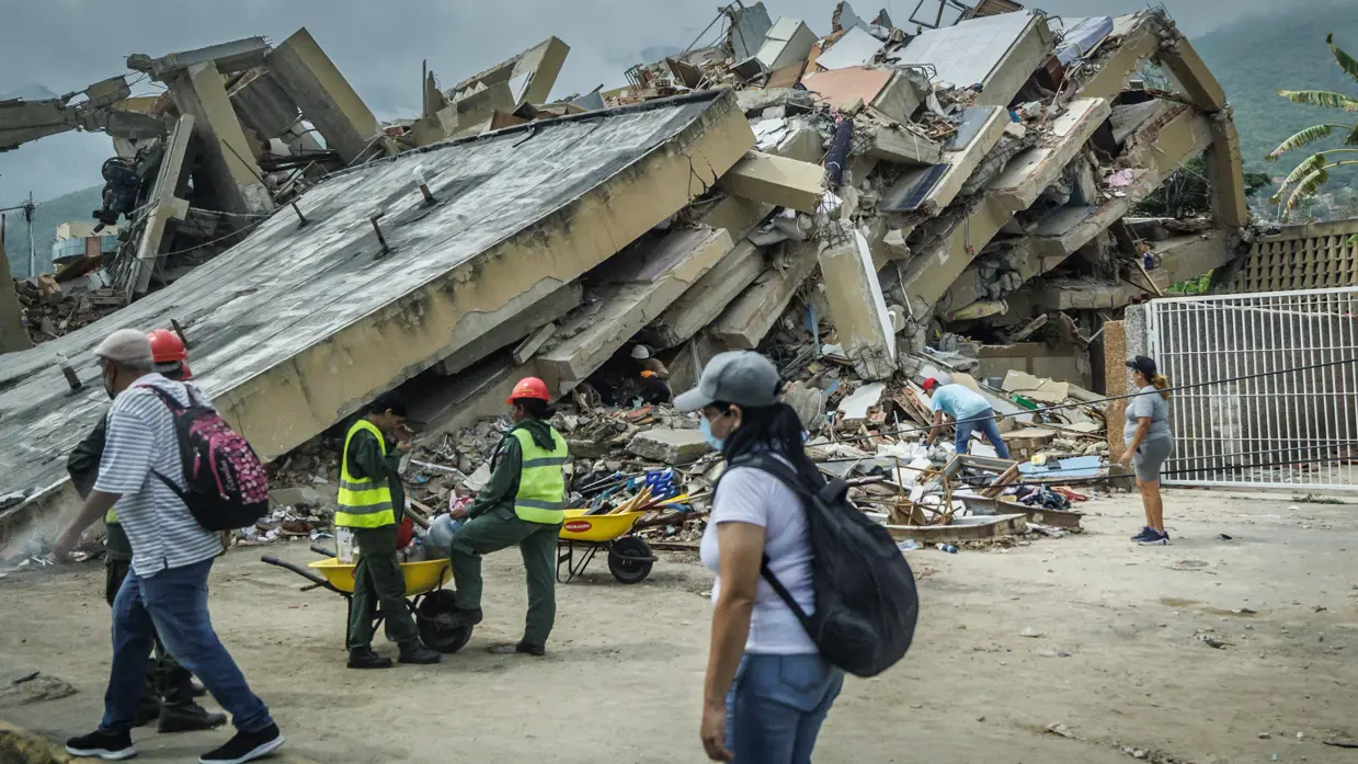 Mensen lopen langs een ingestort gebouwencomplex.