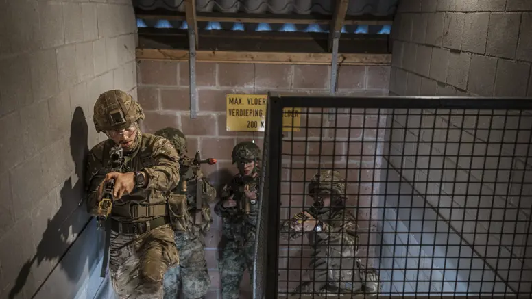Drie soldaten in camouflage met geweren betreden een donkere betonnen ruimte, alert en gericht op een doel.
