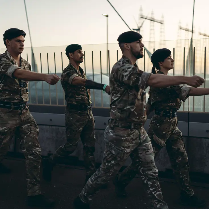 Een groep militairen marcheert over een brug met gestrekte armen.
