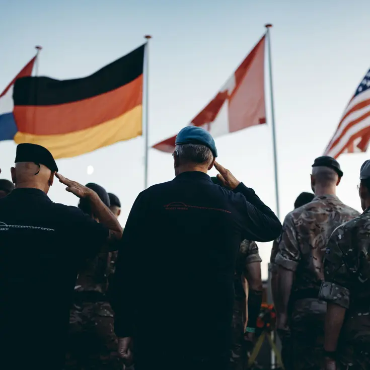 Militairen brengen eregroet, op de achtergrond wapperen vlaggen