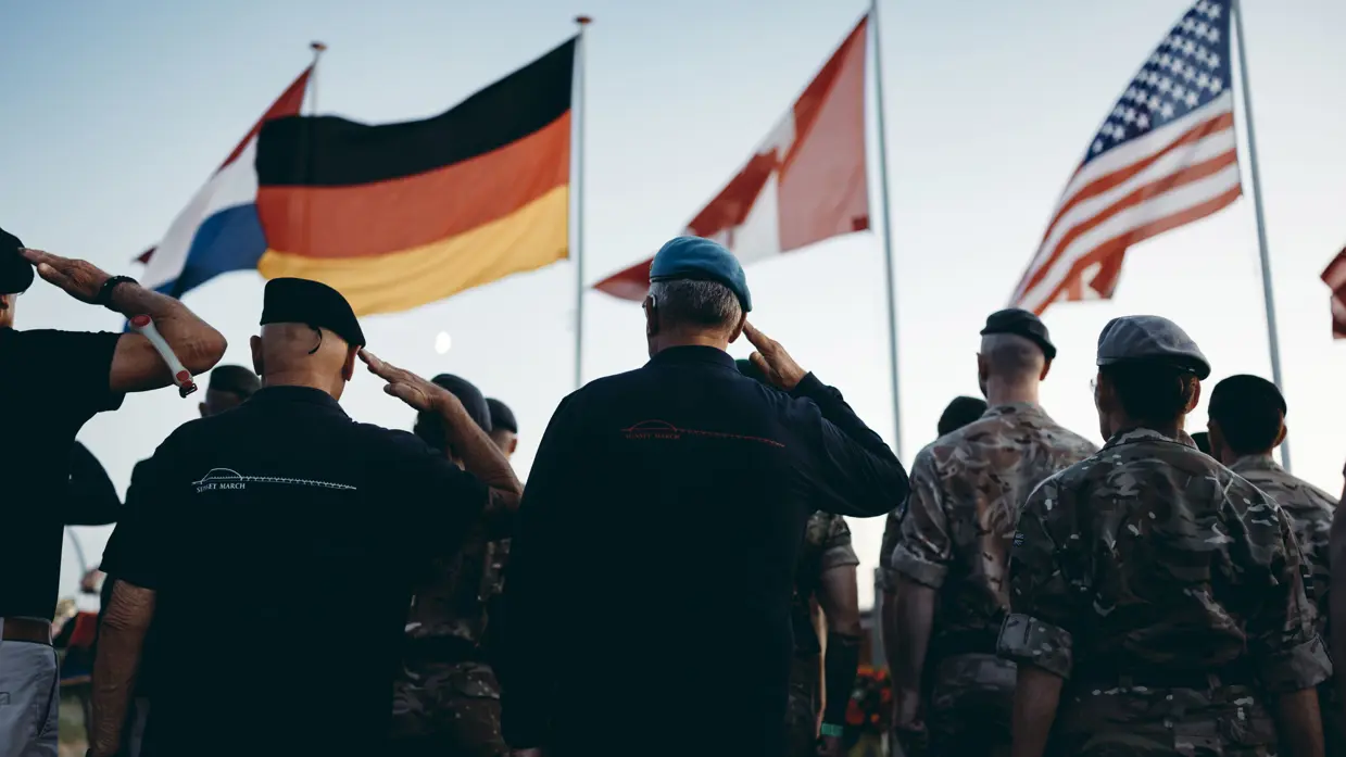 Militairen brengen eregroet, op de achtergrond wapperen vlaggen