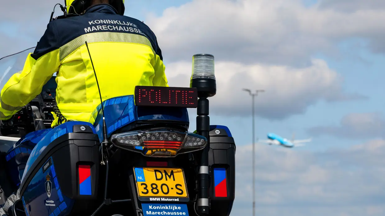 Motorrijder van de Marechaussee, op zijn motor en op de rug gezien met het sein ‘stop’ aan.
