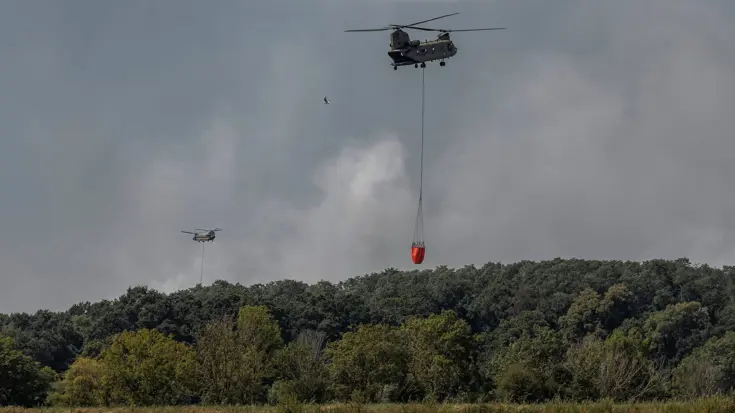 Een Chinook vliegt weg met een volle bambi bucket onder de helikopter.