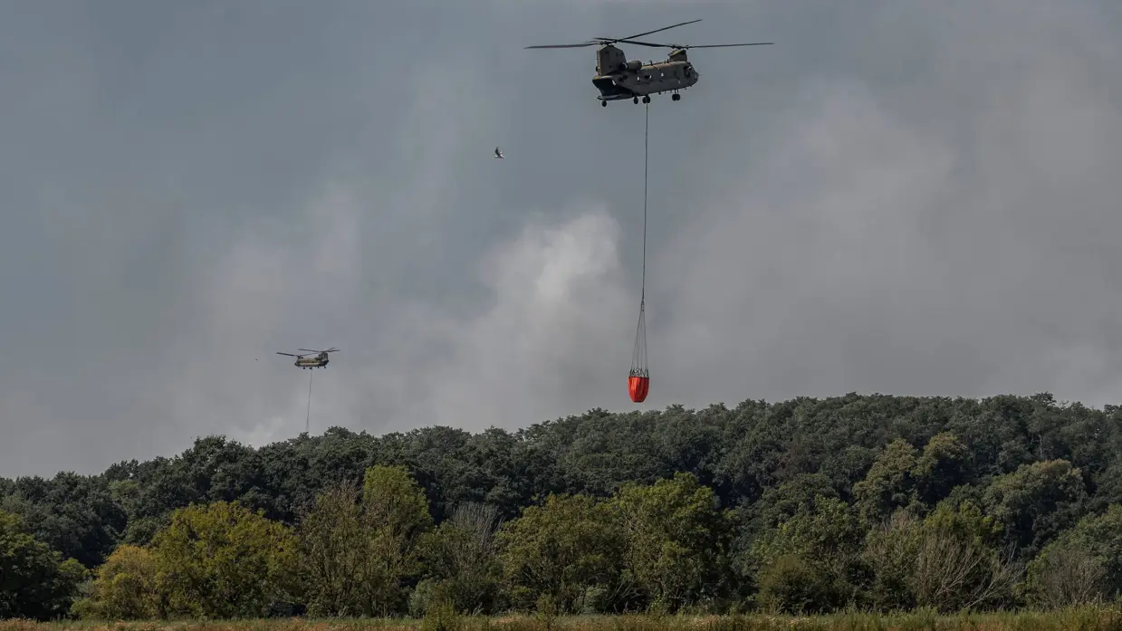 Een Chinook vliegt weg met een volle bambi bucket onder de helikopter.