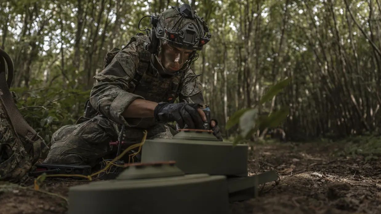 Een genist in het bos maakt een oefenmijn onschadelijk. 