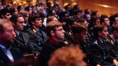 Militairen van verschillende krijgsmachtdelen in hun dagelijks tenue zittend in collegebanken.