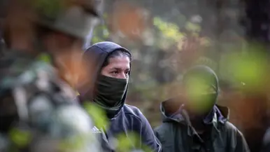 Drie gewapende militairen in gesprek met drie personen in donkere burgerkleding. Een vrouw met een donkere trui en een bedekt gezicht. Militairen in gevecht met de donker geklede partizanen. Twee militairen houden een persoon in burgerkleding vast terwijl diegene met zijn buik op de grond ligt.