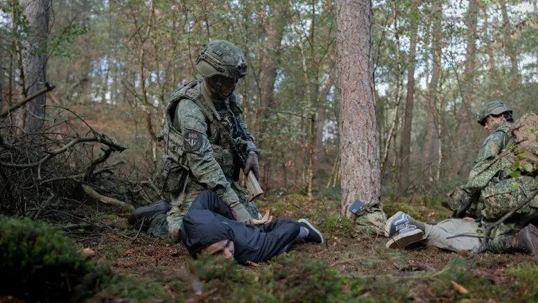  Twee militairen in het bos houden ieder een persoon in burgerkleding tegen de grond gedrukt.