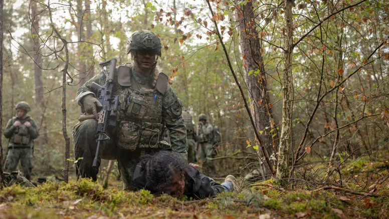 Twee militairen in het bos houden ieder een persoon in burgerkleding tegen de grond gedrukt.