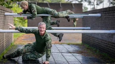 Twee militairen bewegen zich over en onder een obstakel met horizontale palen door. 