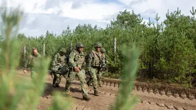 Een groepje militairen tilt een brancard van de grond op een zanderige weg. De militairen lopen met de brancard.