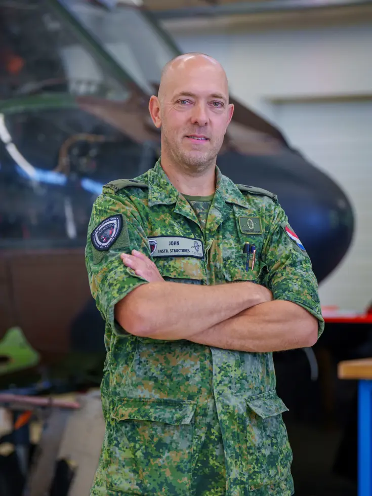 Fotocollage van John Butijn aan het werk als instructeur. Eenmaal heeft hij z’n armen over elkaar en kijkt hij in de camera. Een ander moment helpt hij een leerling bij een aambeeld en zit hij met leerlingen in een gedemonteerde helikopter.