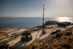 Een groene radar staat op een klif, met verderop een grote antenne en wat legervrachtwagens.