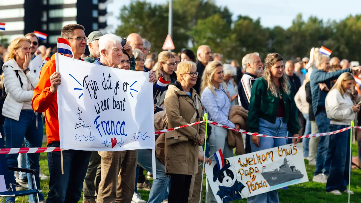 Een grote groep mensen staat aan de kade, enkele van hen houden een spandoek vast.