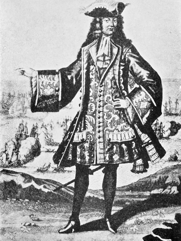 Een man in een weelderig, versierd 17e-eeuws kostuum met een grote pruik, hoed met veren, en een lange jas met ingewikkelde patronen en knopen. Hij staat trots. 