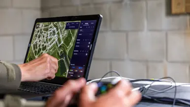 Syl en Lucas kijken naar een scherm, handen op het bedieningsbakje en handen op de laptop    