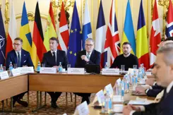 Europese leiders zitten rond een tafel. Vlaggen op de achtergrond.