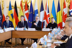 Europese leiders zitten rond een tafel. Vlaggen op de achtergrond.