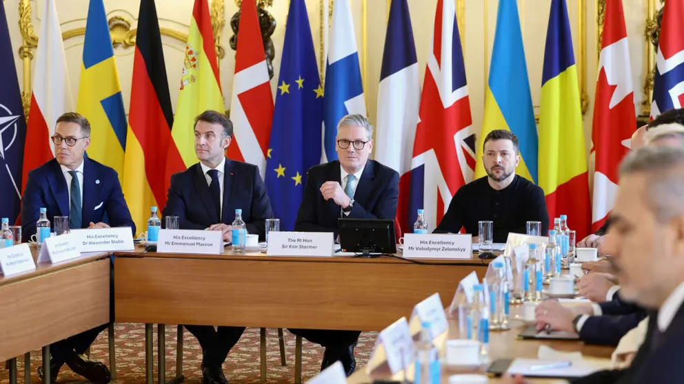 Europese leiders zitten rond een tafel. Vlaggen op de achtergrond.