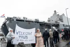 Mensen in regenkleding met spandoek Welkom Thuis bij aankomst marineschip.
