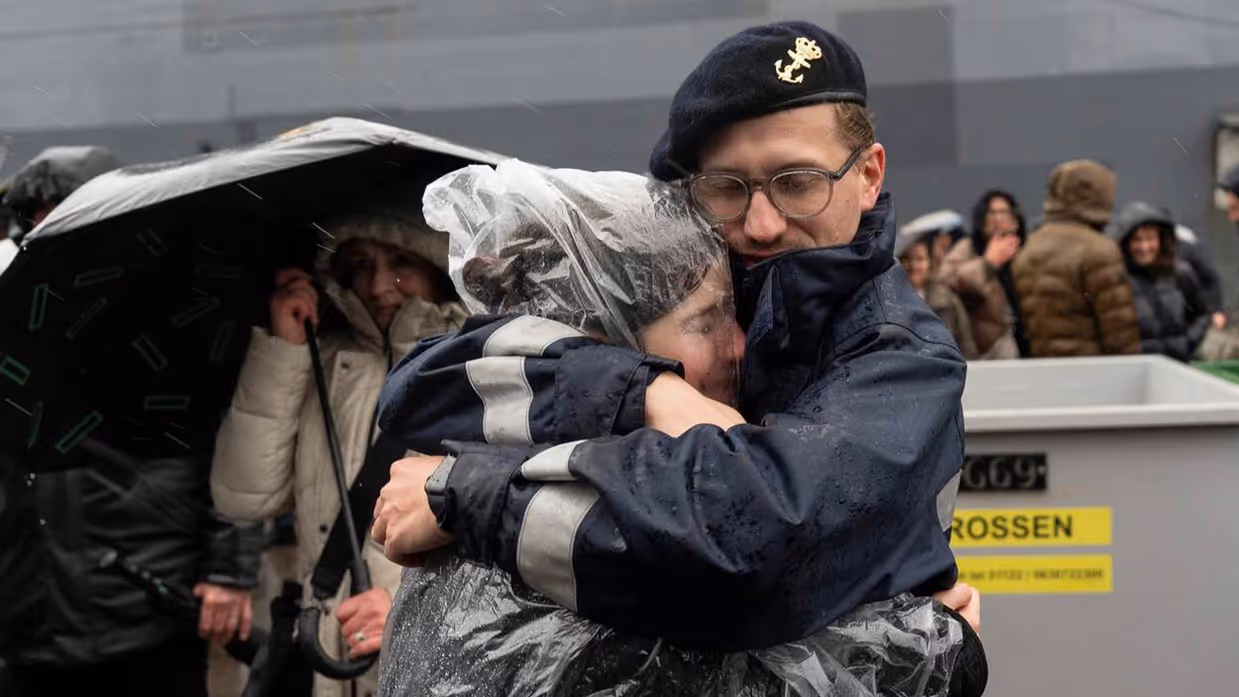 Militair omhelst vrouw in regenkleding innig.