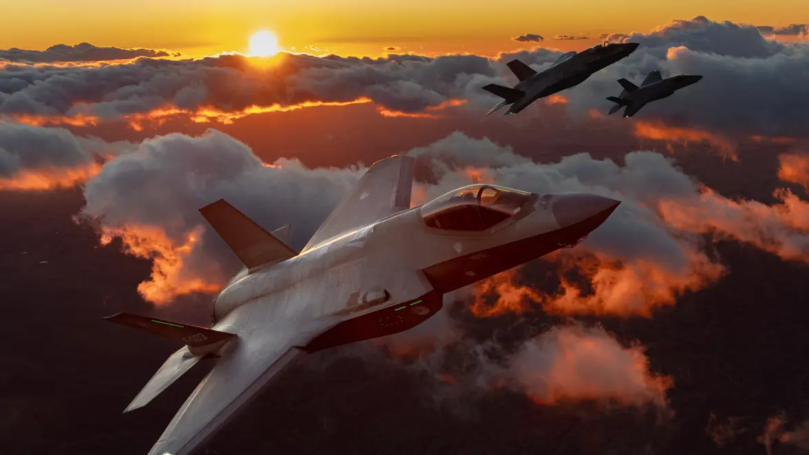 Drie F-35’s boven het wolkendek tegen een oranje lucht met zon.